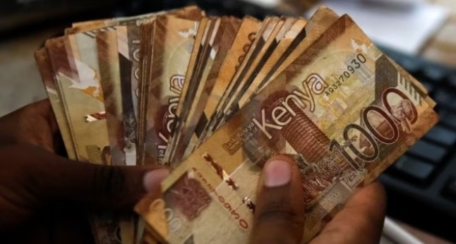 A teller handles Kenya shilling banknotes inside the cashier's booth at an Equity Bank branch